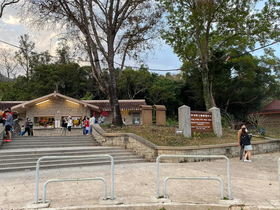 A stone kiosk building with steps and a country park signboard, people walking on the plaza.
