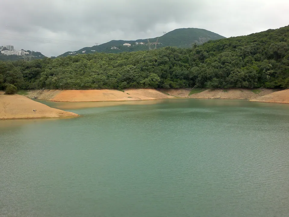 A reservoir with sandy shores below wooded hills.