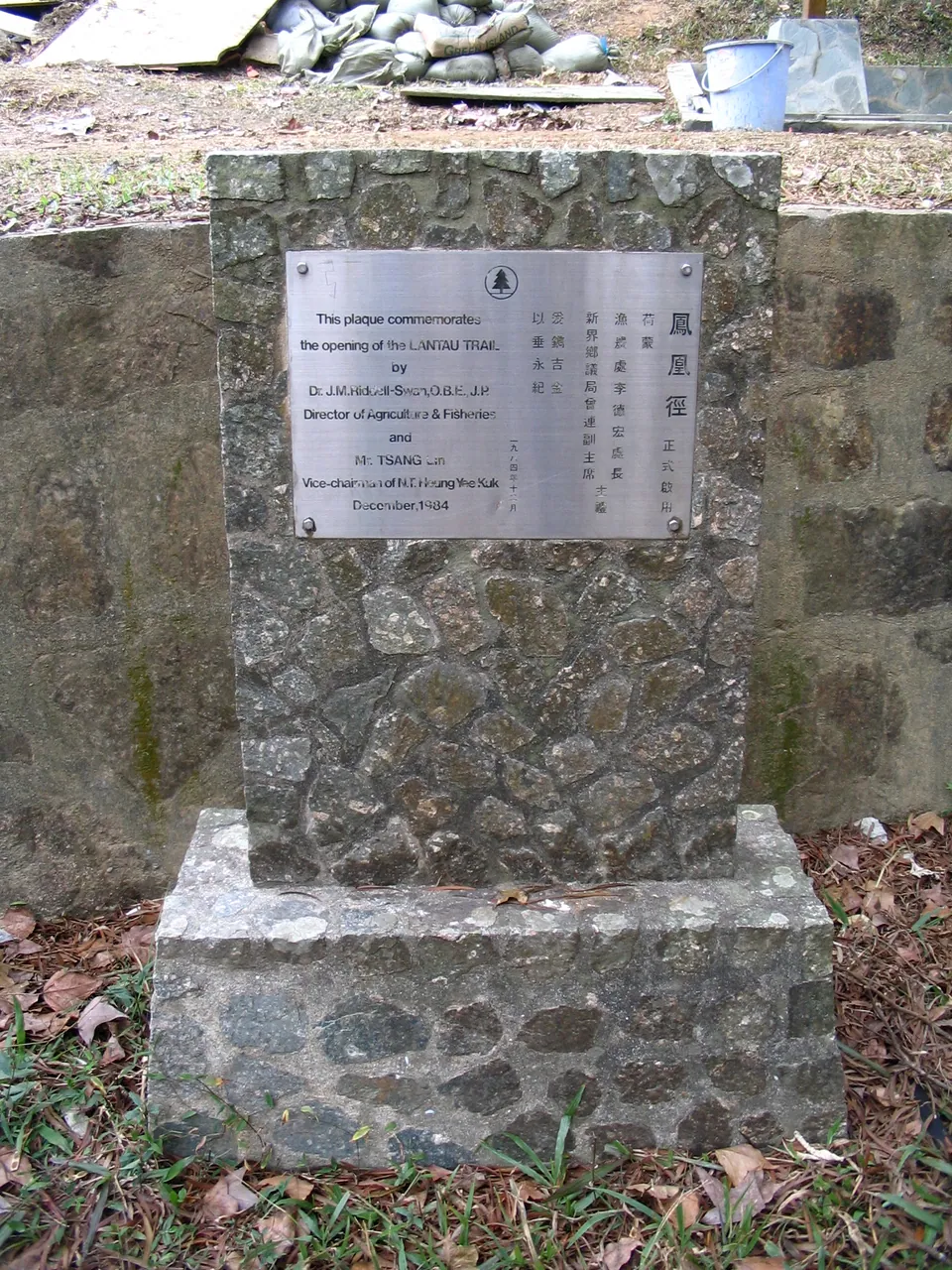 A stone pillar with a metal plaque inscribed in English and Chinese beside the trail.